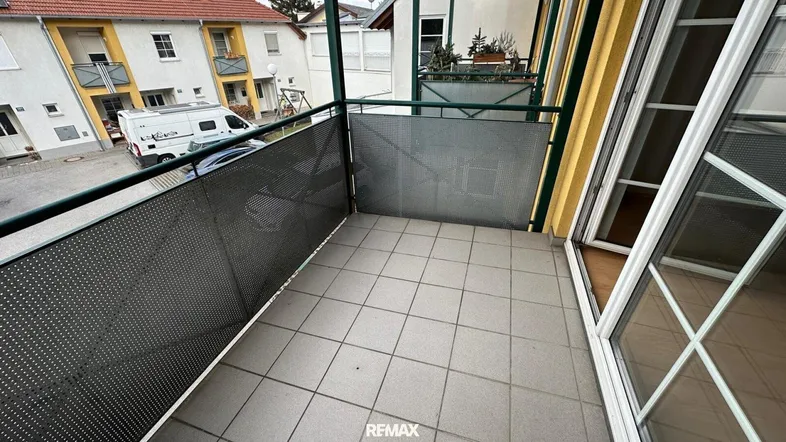 Geräumiger Balkon mit Fliesenboden und Blick auf die umliegenden Gebäude und die Straße.
