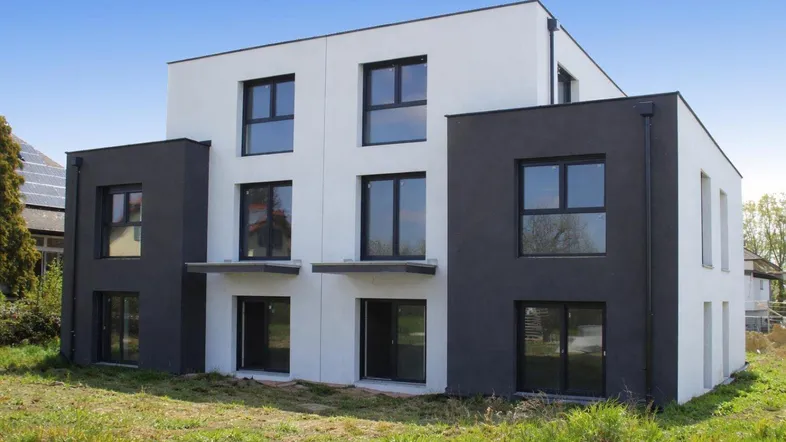 Moderne Doppelhaushälfte mit weißer und dunkelgrauer Fassade, umgeben von einer grünen Wiese.