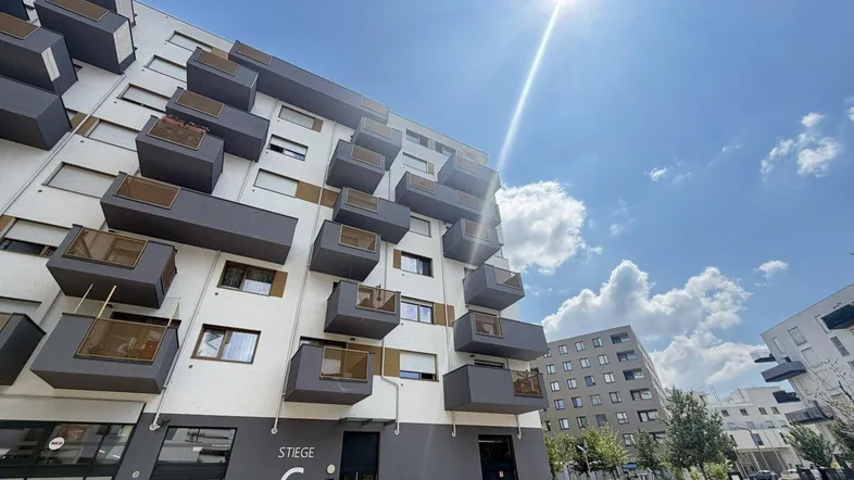 Moderne Wohnanlage mit vielen Balkonen unter strahlend blauem Himmel und Sonnenschein.