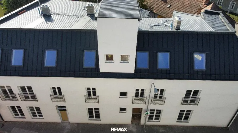 Luftaufnahme eines modernen Gebäudes mit weißer Fassade und dunklem Blechdach.