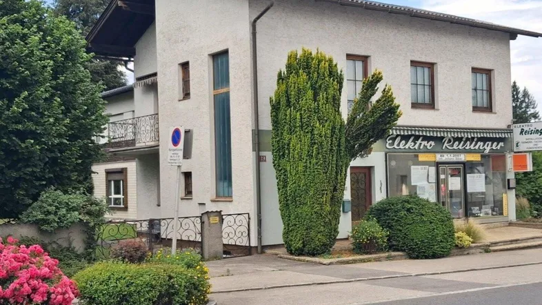 Weißes Mehrfamilienhaus mit Geschäftsfläche im Erdgeschoss und gepflegter Vorgartenbepflanzung.