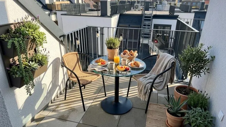 Gemütlicher Balkon mit Frühstückstisch und Blick über die Dächer der Stadt.