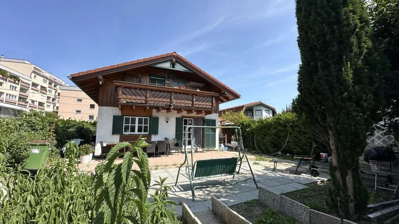 Traditionelles Haus mit Holzfassade, Balkon und großem Garten mit Sitzbereich und Schaukel.