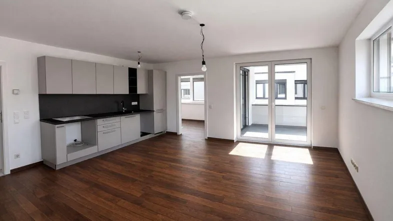 Heller offener Wohn-Essbereich mit integrierter Küche, Parkettboden und Zugang zum Balkon.