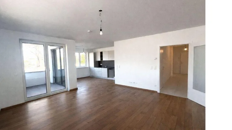 Geräumiger offener Wohn- und Essbereich mit Holzboden und Zugang zum Balkon.