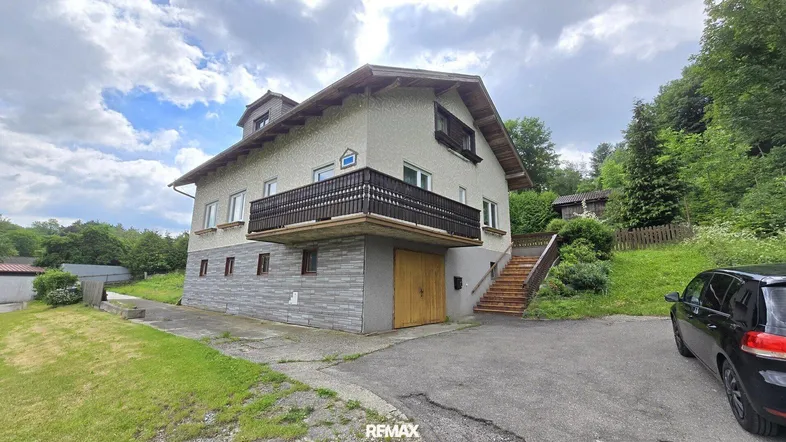 Traditionelles Einfamilienhaus mit Balkon und Garage, umgeben von viel Grün.