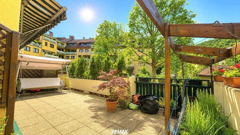 Sonnige Terrasse mit Markise, Schaukelbank und Blick auf die umliegenden Gebäude und viel Grün.