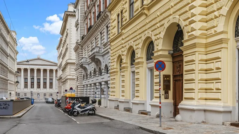 Historische Gebäude entlang einer Straße in Wien mit klassischer Architektur im Hintergrund.
