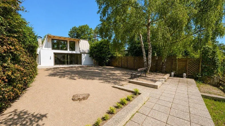 Großzügiger Gartenbereich mit Kiesfläche, Baumbestand und einer modernen Hausfassade im Hintergrund.