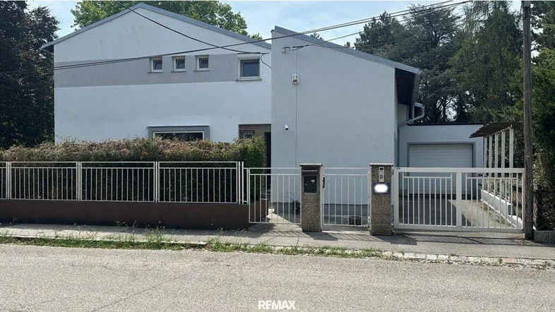 Modernes Einfamilienhaus mit weißer Fassade, umgeben von einem gepflegten Zaun und Hecken.
