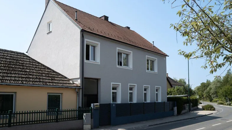 Graues Wohnhaus mit rotem Ziegeldach und gepflegter Fassade an einer Straße gelegen.