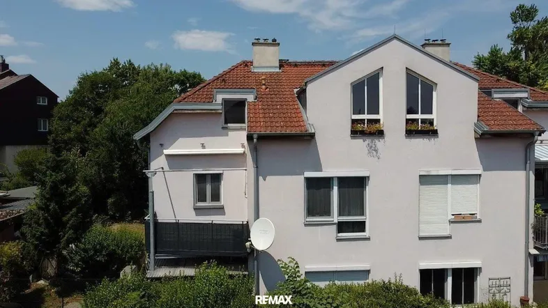 Fassade eines Mehrfamilienhauses mit mehreren Fenstern, Balkon und Satteldach.