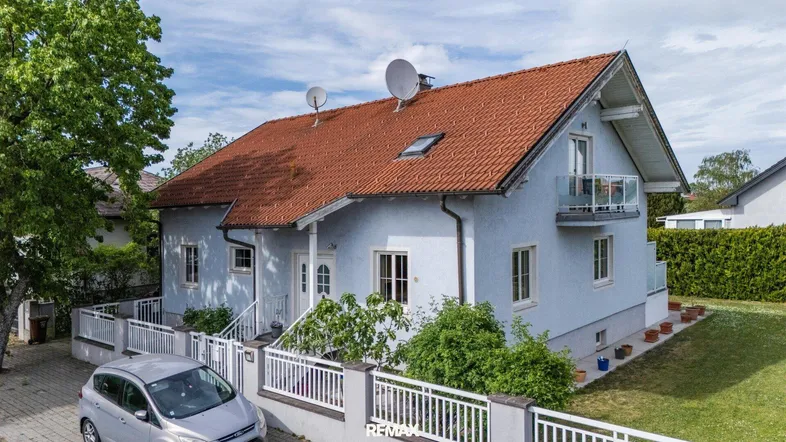 Freistehendes Einfamilienhaus mit hellblauer Fassade, rotem Ziegeldach und kleinem Vorgarten.