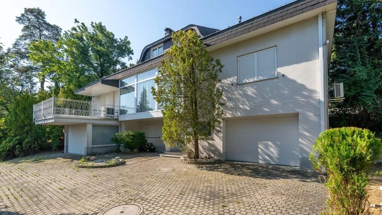 Geräumige Auffahrt führt zu einem großen Haus mit Garage und Balkon, umgeben von viel Grün.