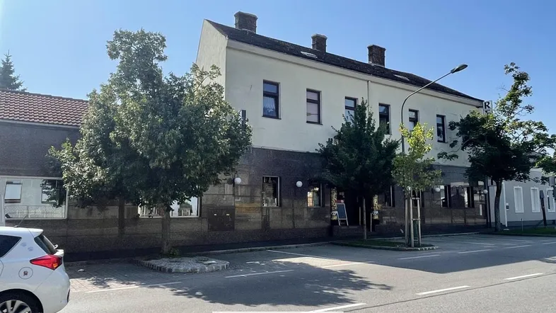 Gebäudeansicht von der Straße mit Bäumen und einem geparkten Auto vor der Fassade.