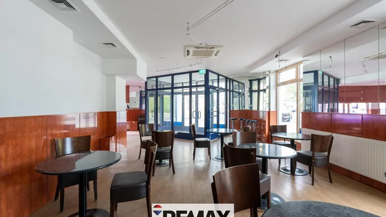 Geräumiger Gewerberaum mit Tischen, Stühlen und einer Glasfront, ideal für Gastronomie.
