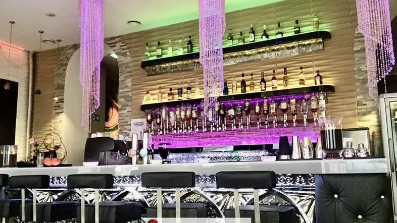 Moderne Bar mit auffälligen Kristallleuchtern, beleuchteten Regalen und einer strukturierten Steinwand.
