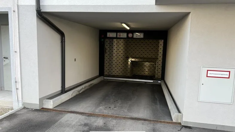 Einfahrt zur Tiefgarage mit geschlossenem Rolltor und modernem Gebäudeeingang.