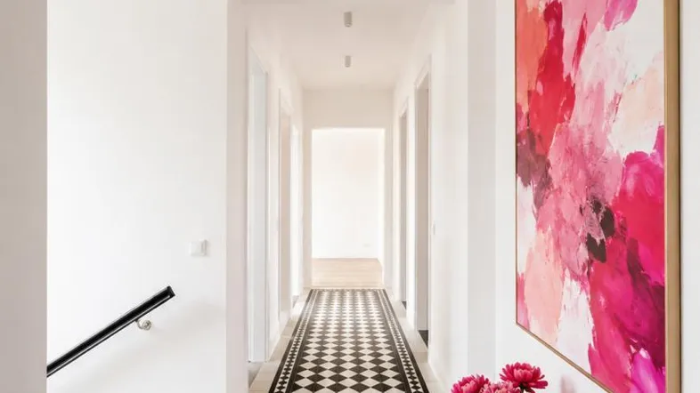 Heller Flur mit auffälligem schwarz-weißem Fliesenboden, moderner Kunst und Zugang zur Treppe.