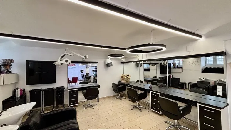 Geräumiger Friseursalon mit mehreren Styling-Stationen, großen Spiegeln und moderner Deckenbeleuchtung.