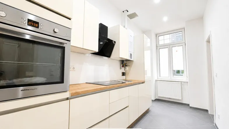Moderne Küche mit hellen Einbauschränken, Holzarbeitsplatte, integriertem Backofen und Fenster.