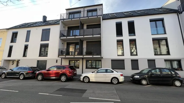 Moderne Wohnhausfassade mit Balkonen und geparkten Autos an der Straße.