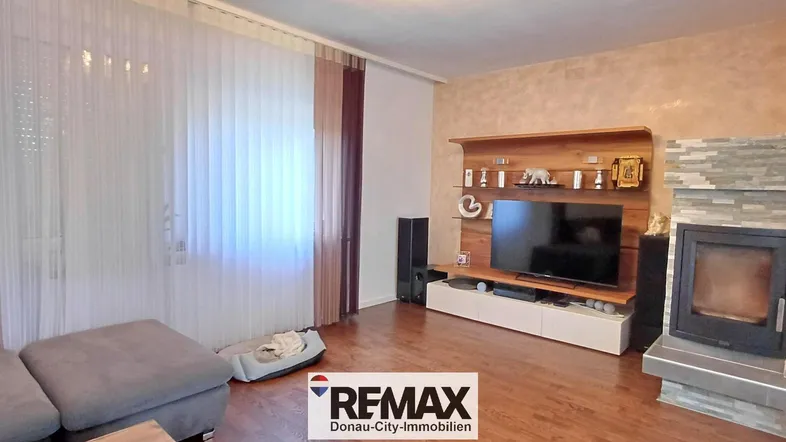Gemütliches Wohnzimmer mit Kamin, Holzboden und großem Fenster für viel Tageslicht.
