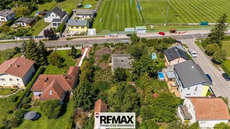 Luftaufnahme eines Grundstücks mit Bestandsgebäude, umgeben von Wohnhäusern und einem Sportplatz.