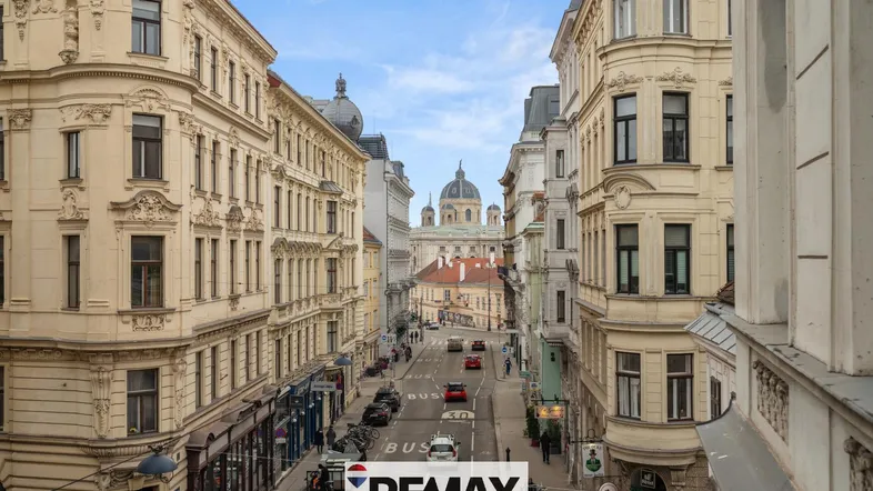 Historische Gebäude säumen eine belebte Straße in der Stadt mit einem markanten Dom im Hintergrund.
