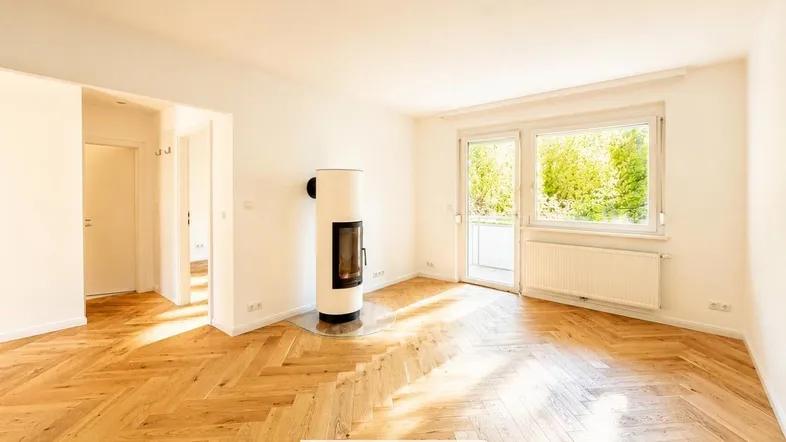 Helles Wohnzimmer mit modernem Kaminofen, Fischgrätparkett und Zugang zu einem Balkon.