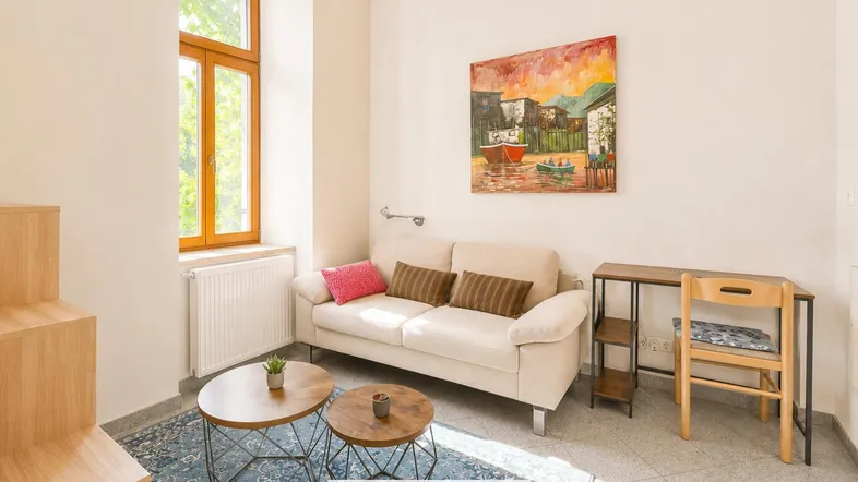 Helles Wohnzimmer mit beigem Sofa, Holztischchen und einem Fenster, das viel Tageslicht hereinlässt.