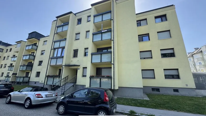 Außenansicht eines Mehrfamilienhauses mit Balkonen und gepflegter Fassade unter hellem Himmel.