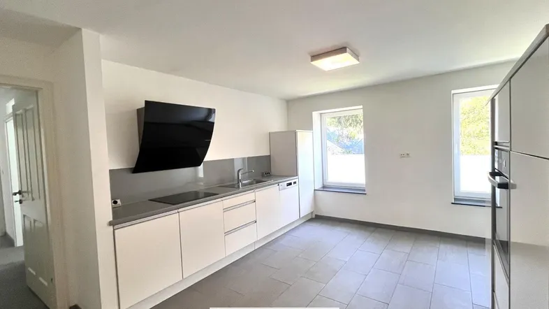 Moderne Küche mit hellen Schränken, Fliesenboden und zwei Fenstern für natürliches Licht.