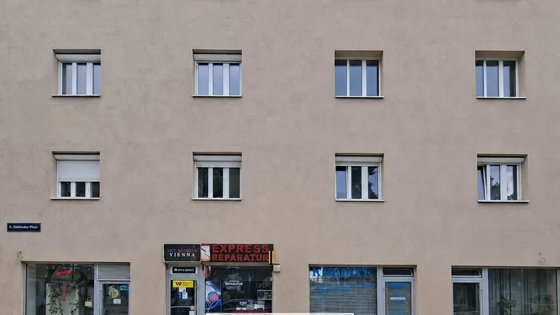 Fassade eines Gebäudes mit mehreren Fenstern und Geschäften im Erdgeschoss, gut gepflegt.