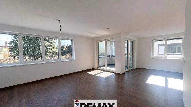 Helles Wohnzimmer mit großen Fenstern, dunklem Boden und Zugang zu einem Balkon.