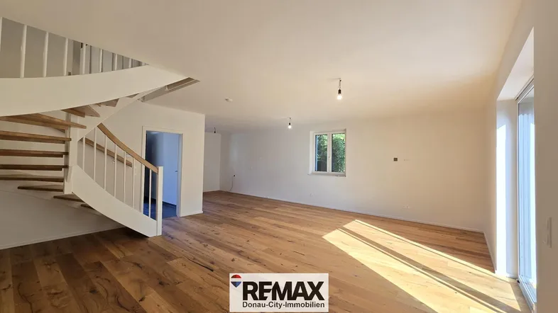 Geräumiger, heller Wohnbereich mit elegantem Holzparkett und geschwungener Treppe, bereit zur Gestaltung.