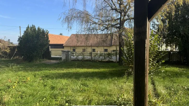 Blick auf ein älteres Gebäude mit Ziegeldach und großem, ungepflegtem Gartenbereich unter blauem Himmel.