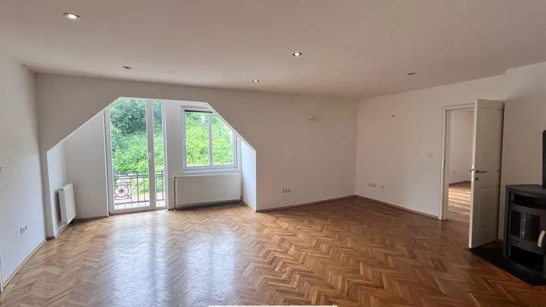 Geräumiges Wohnzimmer mit Fischgrätparkett, Kaminofen und Zugang zu einem kleinen Balkon.