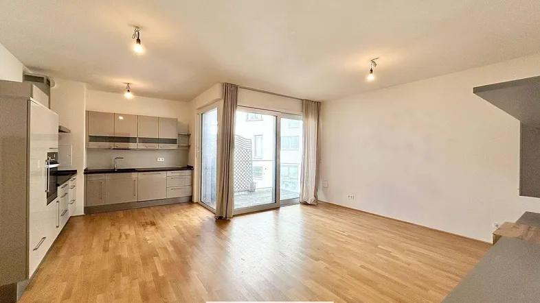 Heller offener Wohn-Essbereich mit integrierter Küche, Parkettboden und Zugang zur Loggia.