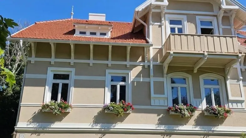 Elegante Fassade eines historischen Gebäudes mit Blumenkästen und dekorativen Elementen unter blauem Himmel.