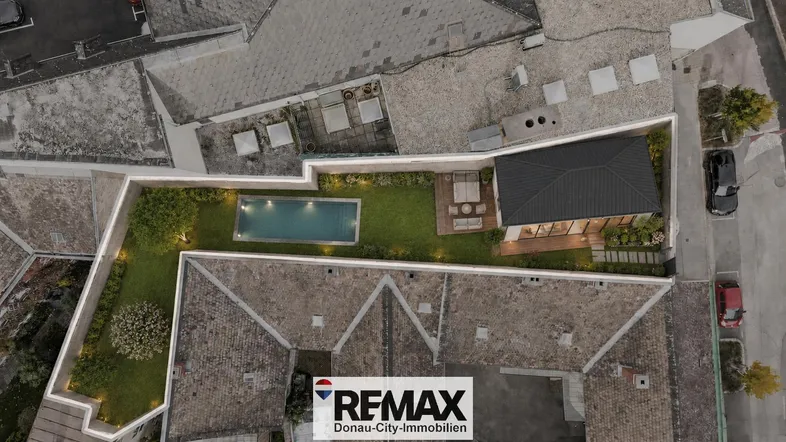 Luftaufnahme eines Anwesens mit modernem Haus, Garten und Swimmingpool, umgeben von Dächern.