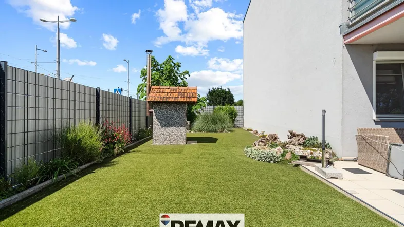 Gepflegter Gartenbereich mit Kunstrasen, Grillplatz und einer kleinen Steinhütte neben dem Haus.