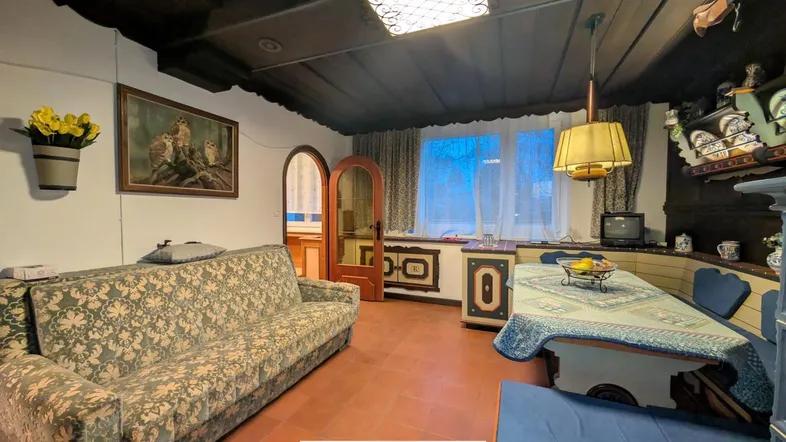 Traditioneller Wohn- und Essbereich mit dunkler Holzdecke, gemustertem Sofa und gefliestem Boden.