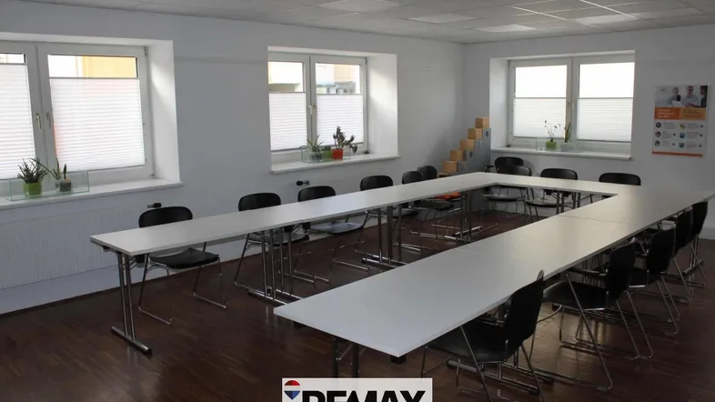 Großer Konferenzraum mit U-förmiger Tischordnung, Holzfußboden und mehreren Fenstern für Tageslicht.