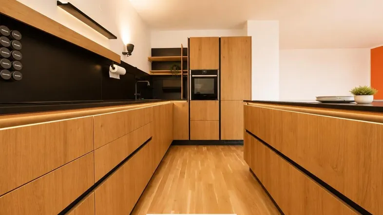 Moderne Küche mit Holzfronten, schwarzer Arbeitsplatte und integrierten Geräten, beleuchtet durch LED-Streifen.