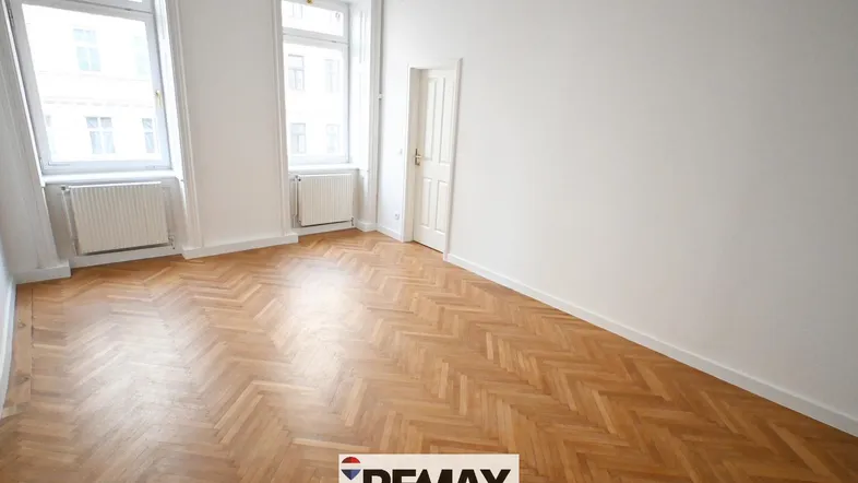 Helles, leeres Zimmer mit Fischgrätparkettboden und großen Fenstern, bereit zur individuellen Gestaltung.