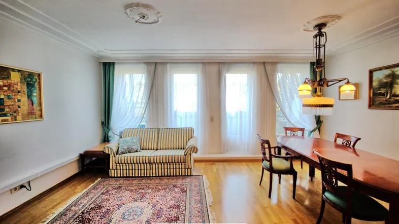 Helles Wohn- und Esszimmer mit Parkettboden, Stuckdecke und großen Fenstern.