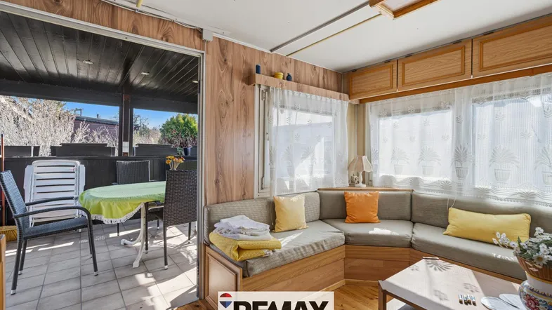 Gemütlicher Wohnbereich in einem Mobilheim mit Ecksofa und Zugang zu einer überdachten Terrasse.