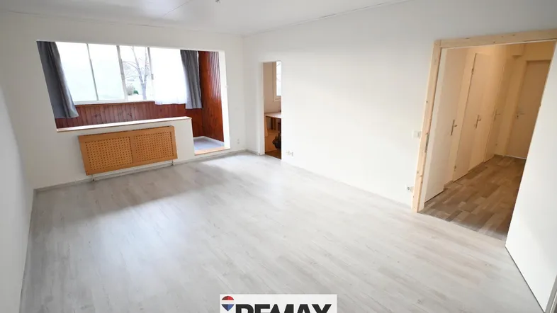 Helles Wohnzimmer mit hellem Laminatboden und einem angrenzenden Bereich mit Holzverkleidung und Fenster.
