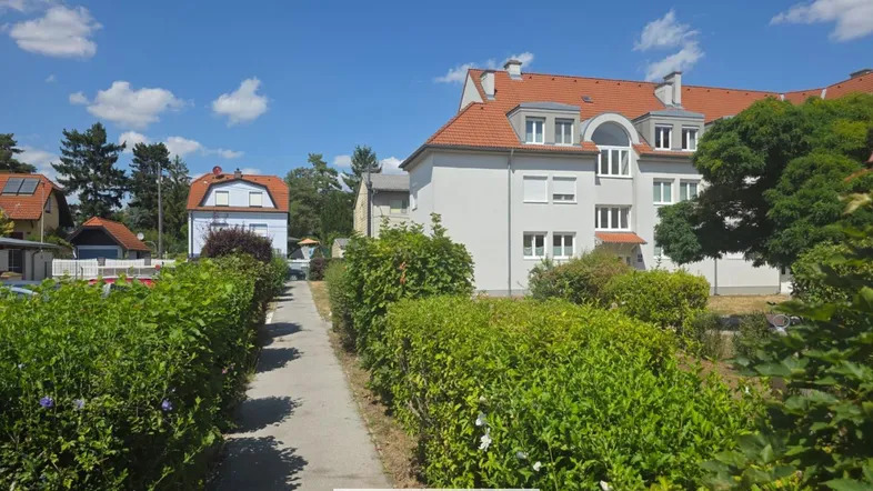 Mehrfamilienhaus mit gepflegter Außenanlage und Hecken entlang des Gehwegs unter blauem Himmel.